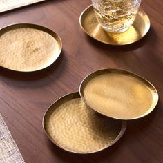 three gold dishes sitting on top of a wooden table next to a glass filled with liquid