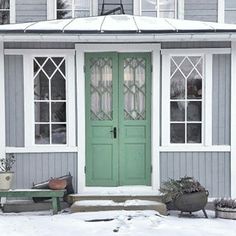 a green front door sitting next to a white bench in front of a gray house