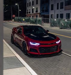 a red chevrolet camaro is parked on the side of the road at night time