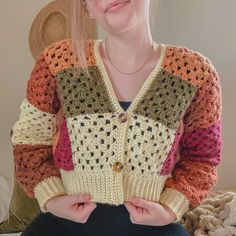 a woman sitting on a bed wearing a multicolored cardigan