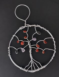 a wire tree with red and white beads hanging from it's center, on a black surface