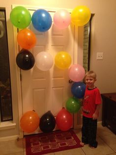 a young boy standing in front of a door with balloons