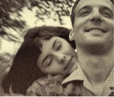 a man and woman standing next to each other under a tree with their eyes closed