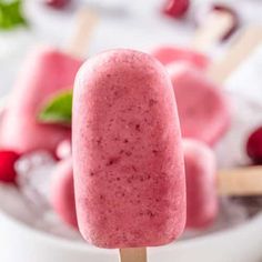 a close up of a popsicle on a stick with raspberries in the background