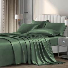 a bed with green sheets and pillows in a room next to a lamp on a nightstand