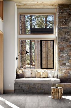 a living room filled with lots of windows next to a stone wall and wooden floor