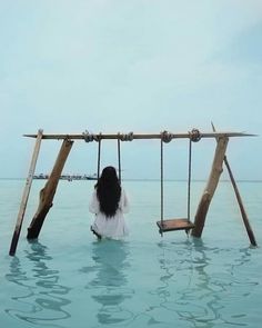 a woman sitting on a swing set in the middle of the ocean with her back to the camera