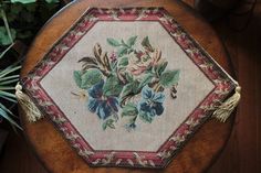 a wooden stool with a flowered design on it's side and a plant in the background