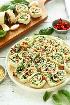 spinach rolls on a white plate with red peppers and seasoning next to them