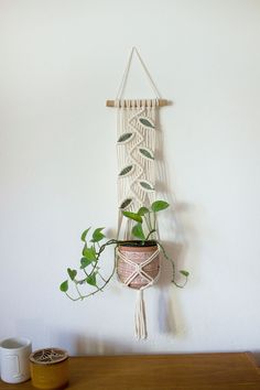 a macrame plant hanging on a wall next to a coffee cup and mug