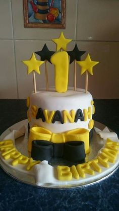 a birthday cake with yellow and black icing, stars on top that say happy birthday