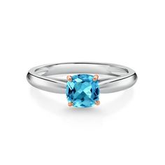 a cushion cut blue topazte ring with two tone gold accents on the band