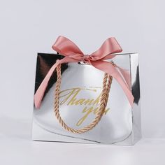 a silver shopping bag with a pink ribbon tied around the handle that says thank you