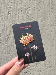 a hand holding a black card with flowers on it and spider - lily in the center