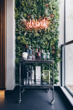 a bar cart sitting in front of a wall covered with greenery and neon signs