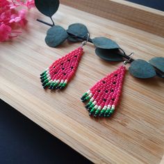 a pair of pink and green beaded watermelon earrings sitting on top of a wooden table