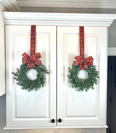 two christmas wreaths hanging from the front of white cabinets