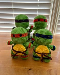 three crocheted ninja turtles sitting next to each other on top of a wooden table