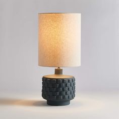 a black table lamp with a white shade on it's base and a light bulb in the middle