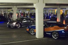 two cars parked in a parking garage with people standing around the car and looking at them