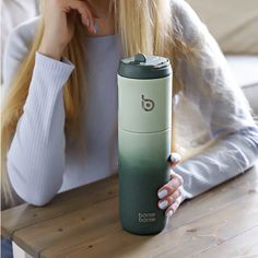 a woman sitting at a table with a green and white coffee cup