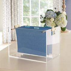 a blue file box sitting on top of a white table next to a vase with flowers