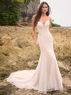 a woman in a wedding dress standing on rocks near the ocean with her hand on her hip