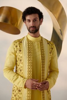 Summer Love Shrug Set | Jatin Malik Introducing our vibrant lemon yellow shrug set, adorned with intricate floral hand embroidery and three types of embroidered lapels in shades of yellow. This ensemble radiates freshness and sophistication, capturing attention with its intricate detailing and vibrant color palette. Paired with an embroidered shoulder-button kurta and tapered trousers, this outfit offers a perfect balance of elegance and contemporary style. Ideal for special occasions, this ensemble is sure to make a statement with its unique design and impeccable craftsmanship. Included in purchase: Shrug Set, Kurta, Trousers Product Specification Color: Yellow Fabric: Linen Silk Occasion: Engagement, Wedding, Bridal, Reception Style: Shrug Set, Kurta, Trousers Care: Dry Clean Work: Hand Yellow Bandhgala With Chikankari Embroidery, Yellow Long Sleeve Bandhgala With Chikankari Embroidery, Festive Yellow Kurta With Intricate Embroidery, Festive Yellow Sets With Intricate Embroidery, Yellow Embroidered Kurta For Diwali, Yellow Bandhgala With Zari Work And Long Sleeves, Yellow Bandhgala With Resham Embroidery Long Sleeve, Yellow Long Sleeve Bandhgala With Zari Work, Yellow Long Sleeve Bandhgala With Resham Embroidery