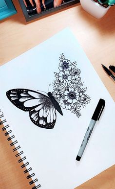 a drawing of a butterfly and flowers on a white paper next to a black marker