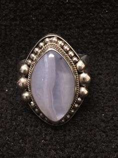 Ring ~ Blue Lace Agate Artist: John Binzley Blue Lace Agate Cabochon Heavy Gage Sterling Silver Size: 6 1/2 Length: 1 1/8 Width: 3/4 Solid Silver Back $280- Blue Lace Agate has a soft, soothing elegance; like sky-blue waters released from winters grasp. Its graceful, circular Fine Jewelry Agate Gemstone, Elegant Blue Oval Cabochon Moonstone Ring, Luxury Silver Cabochon Gemstones, Oval Chalcedony Fine Jewelry, Formal Jewelry With Natural Chalcedony Stones, Elegant Oval Agate Jewelry, Formal Chalcedony Jewelry With Natural Stones, Oval Blue Agate Jewelry, Blue Oval Agate Jewelry