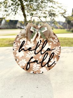 a wooden sign that says hello fall with leaves on it and a bow hanging from the front