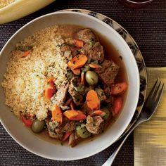 a white bowl filled with meat and vegetables next to a glass of wine on top of a table