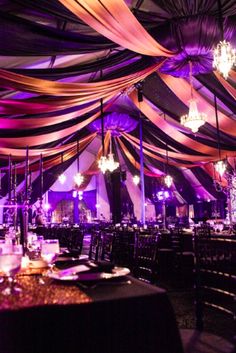 a banquet hall decorated with purple and white draping, chandeliers and tables