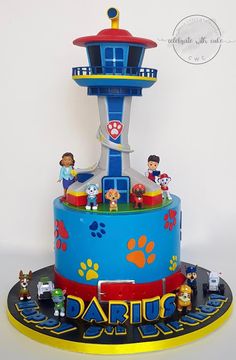 a blue and yellow cake with paw patrol figures on it's bottom tier, in front of a white background