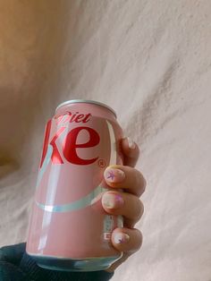 a woman holding up a pink diet coke can with white and blue designs on it