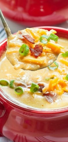 a spoon full of soup with bacon and green onions on it, in a red bowl