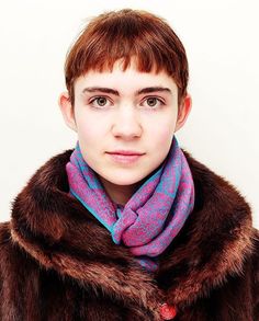 a woman wearing a fur coat with a pink and blue scarf around her neck is looking at the camera