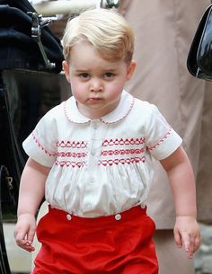 a little boy in a white shirt and red skirt is standing next to a man