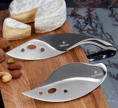 two knives sitting on top of a wooden cutting board next to some nuts and cheese