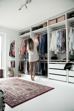 a woman standing in front of a closet full of clothes and other items on shelves