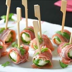 small appetizers with toothpicks are arranged on a white plate and garnished with green leaves