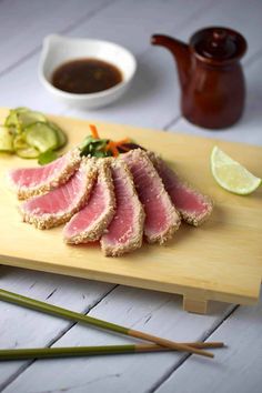 sliced meat and vegetables on a cutting board with chopsticks next to the plate