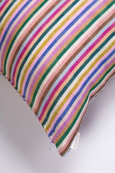 a multicolored striped pillow on a white surface with a tag in the corner