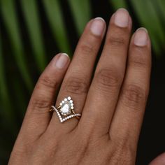 a woman's hand with a diamond ring on top of her finger and a green leaf in the background