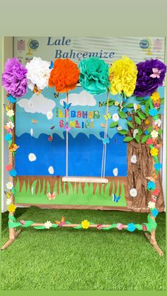 a colorful display with flowers and trees on the grass in front of a bulletin board