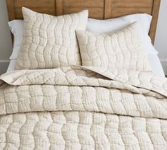 an unmade bed with white linens and pillows on top of the headboard