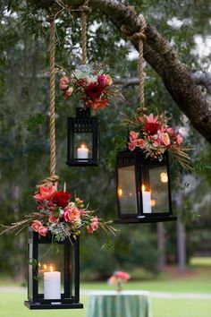 three hanging lanterns with flowers and candles on them are hung from a tree in the woods