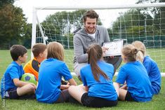 a man sitting in front of a group of kids on a field with a soccer ball