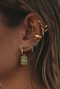 a close up of a person wearing ear cuffs and piercings with green stones on them