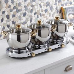 four silver pots and pans sitting on top of a counter next to a book